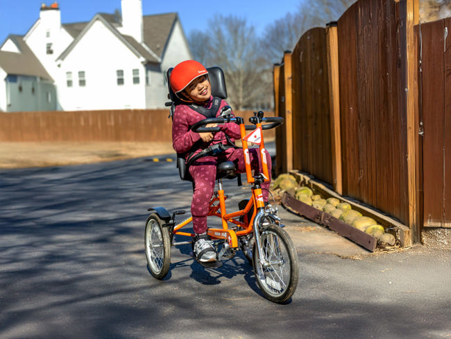 A child riding an orange DCP16 adaptive tricycle