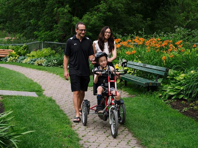 A family walking beside a rider on a red adaptive tricycle