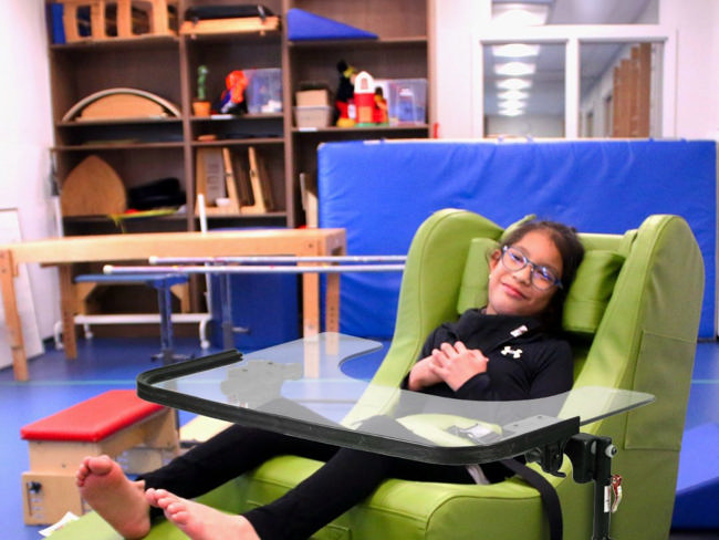A girl relaxing in a green Chill-Out Chair with an activity tray