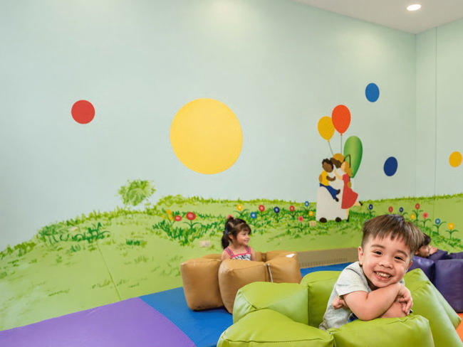 Young children playing on soft green positioning pieces in a bright playroom